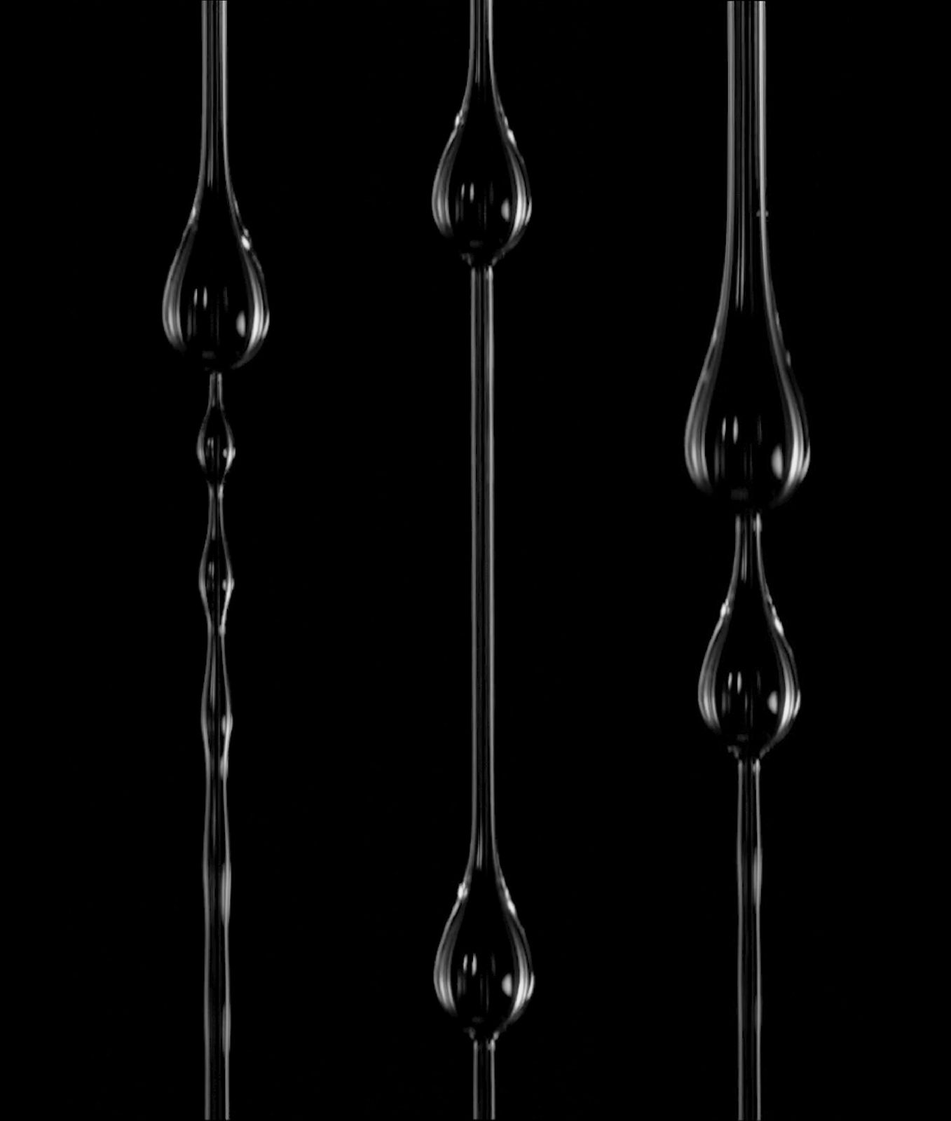Three vertical fibers coated with liquid that has broken into glistening beads, on black.