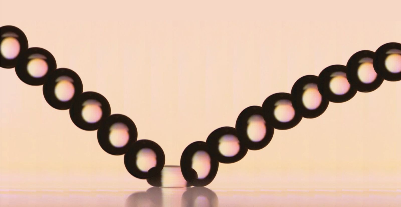A sequence of drop positions tracing a V as a drop bounces off a surface, on a peach background.