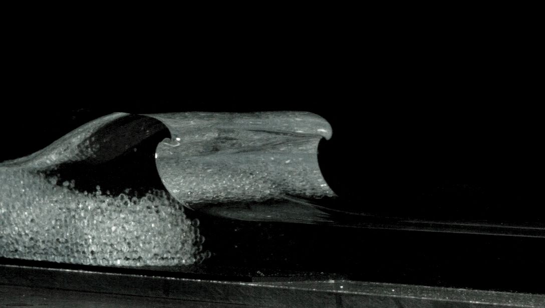 A wave curling over as it begins to break, on a black background.