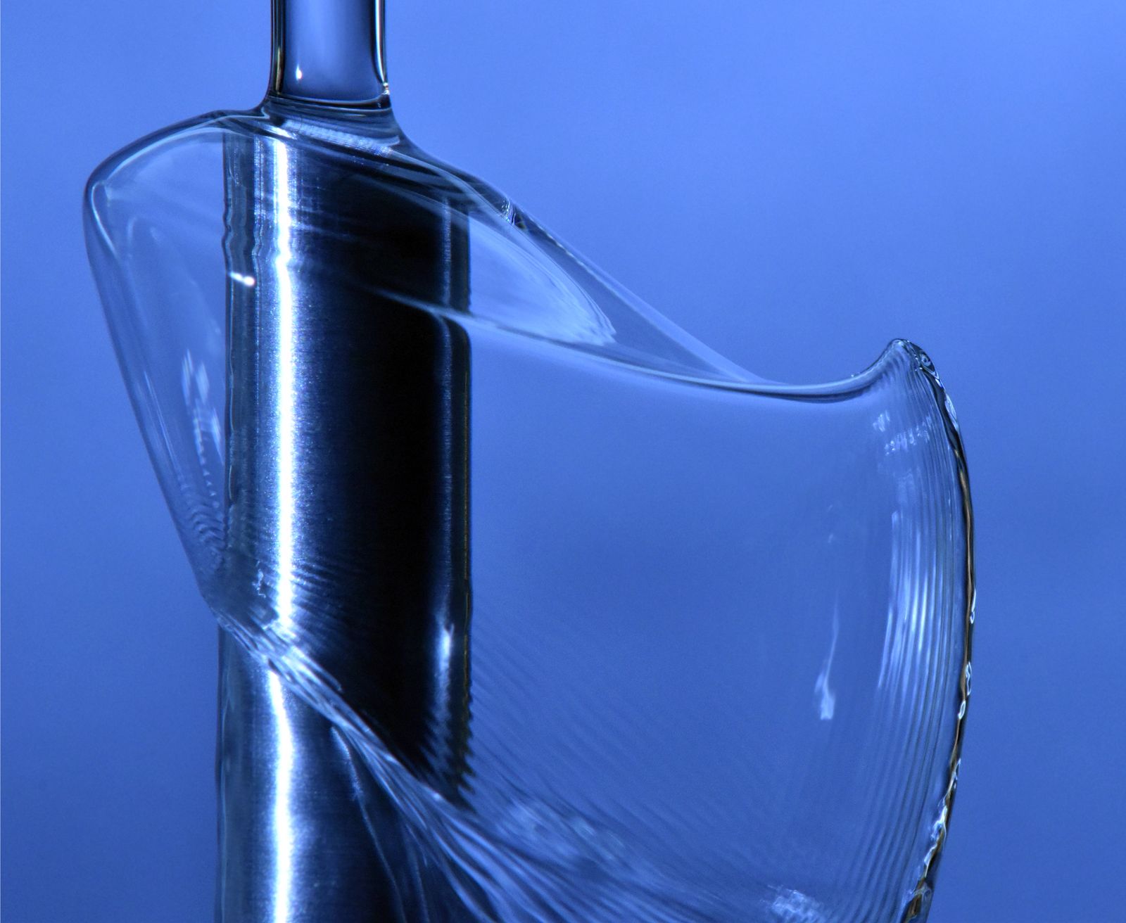 A clear liquid sheet curving sharply around a vertical jet against a blue background.